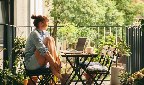Person sitting on a small balcony with plants and a warm drink